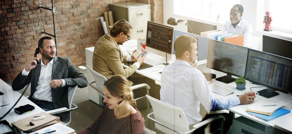 Eine Gruppe von fünf Mitarbeitern diverser Ethnien und Geschlechter sitzt in hippem, hellem Büro