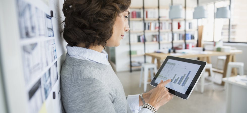 Adrette Business-Frau steht in Tageslicht-Büro und bedient ein Tablet
