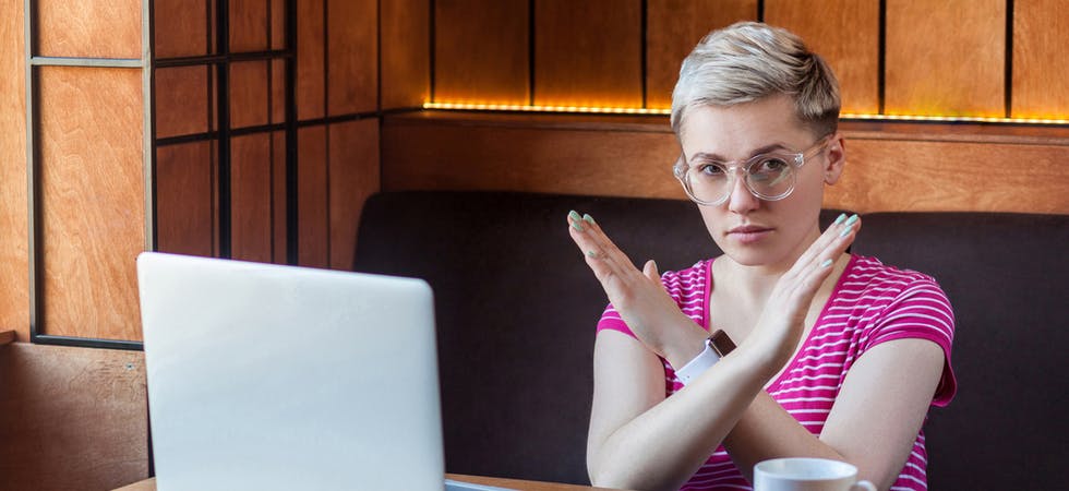 Eine junge Frau mit kurzen, blonden Haaren kreuzt verneinend die Arme vor der Brust, sitzt vor einem Laptop