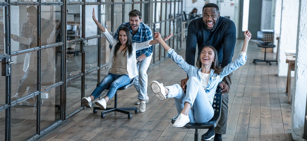 Junge Arbeitskollegen veranstalten ein Bürostuhl-Rennen im modernen Office