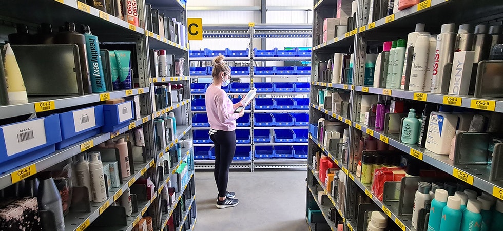 Eine junge Frau steht in einem Lager mit vielen Kosmetikprodukten